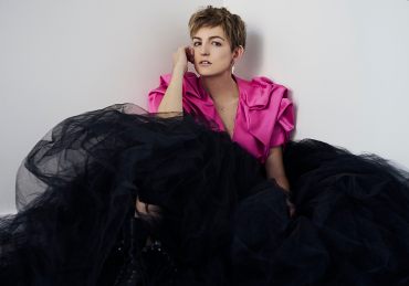 Natural light portrait portrait of a young woman wearing a structural pink crop jacket and large black tulle skirt with combat boots looking directly at the camera