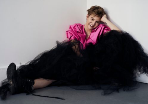 Natural light portrait portrait of a young woman wearing a structural pink crop jacket and large black tulle skirt with combat boots laughing at the camera