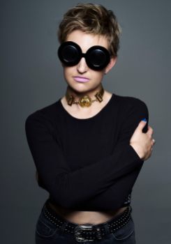 Studio portrait of a young woman with blonde hair wearing large black sunglasses and mauve lipstick
