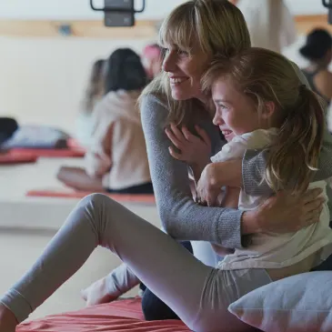 A woman sits on the floor smiling hugging her smiling daughter on her lap during a mother and daughter workshop in Vancouver focusing on relationships and self care